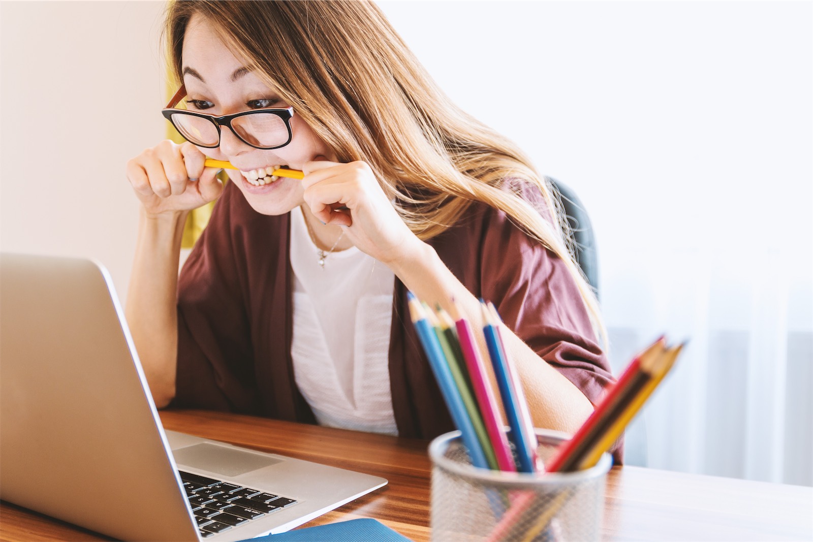 The picture shows a young Asian woman with black glasses in front of a laptop. She is visibly annoyed, as she bites theatrically into a pencil. To prevent this situation, you can unlock the Power of a Learning to supercharge Staff Engagement in 2023!
